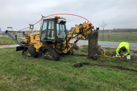 Kabelpflug der auf eine Wiese die Erde zur Verlegung des Kabels aufpflügt. Ein Mann arbeitet bei der Verlegung mit.