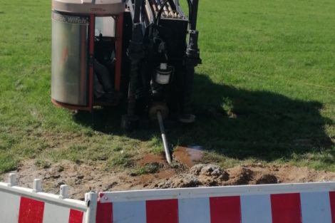 Spülbohrer in Rot auf einer Wiese von vorn. Im Vordergrund eine Baustellenabsperrung.