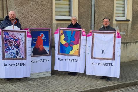 3 Personen zusammen vor einem zum Kunstkasten verhüllten Netzverteiler an einer Straße in Königswartha. Die Personen präsentieren 3 weitere "Kunsthüllen".