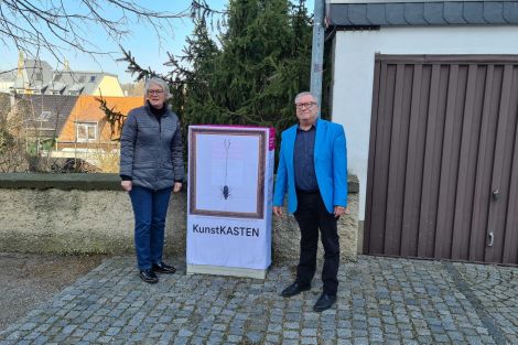 2 Personen zusammen vor einem zum Kunstkasten verhüllten Netzverteiler an einer Straße in Radeberg..