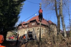 3 Bauarbeiter verlegen ein Kabel an einem Mast.